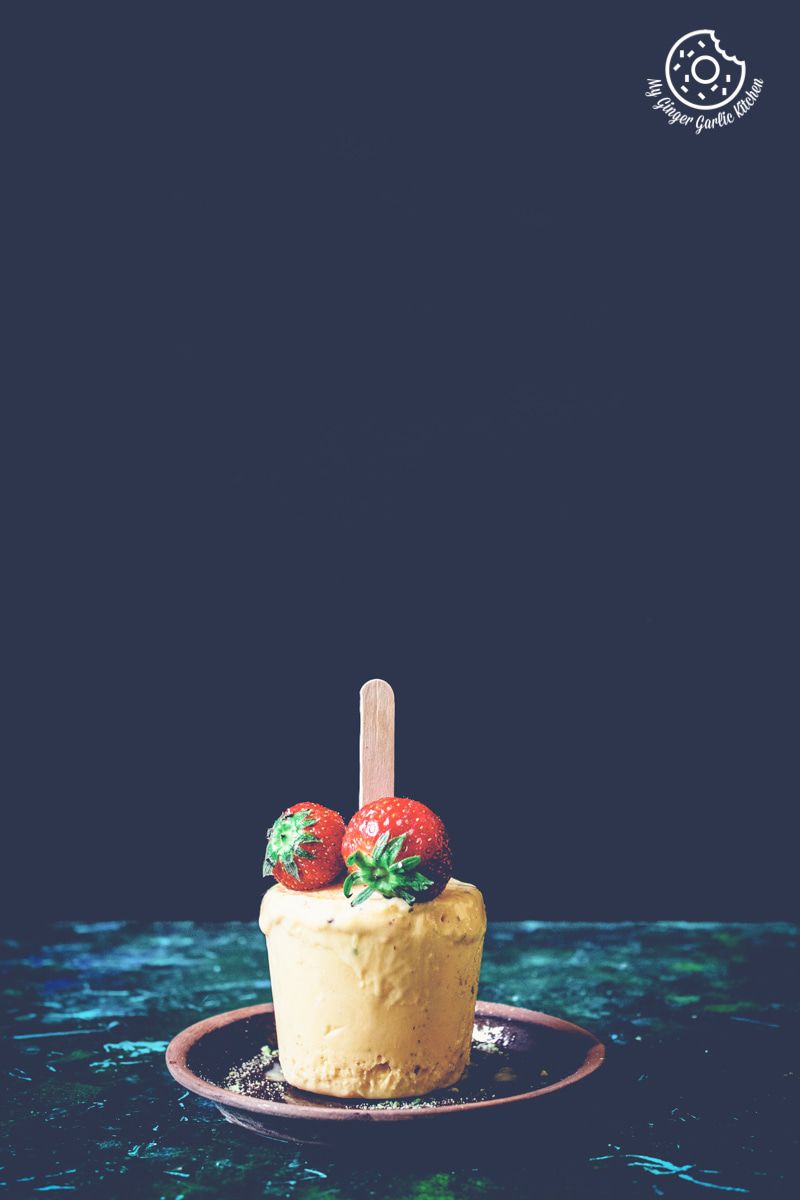 there is a mango kulfi with strawberries on top of it on a plate