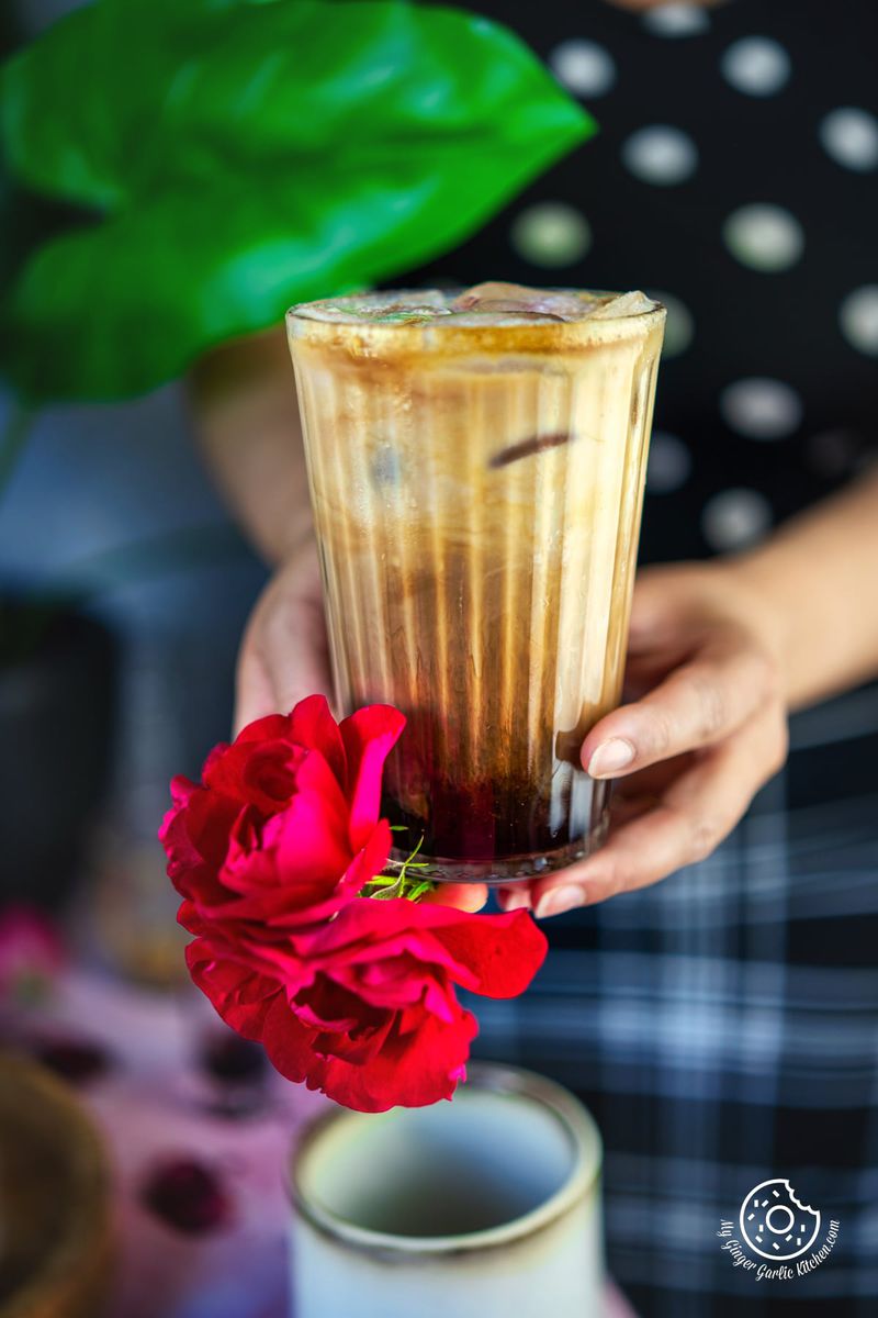 A hand is holding a glass of iced rose latter and a bunch red roses.