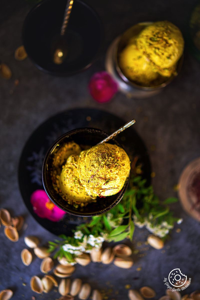 overhead shot of two kesar pista ice cream scoops in a small black bowl with an ice cream bowl on the side