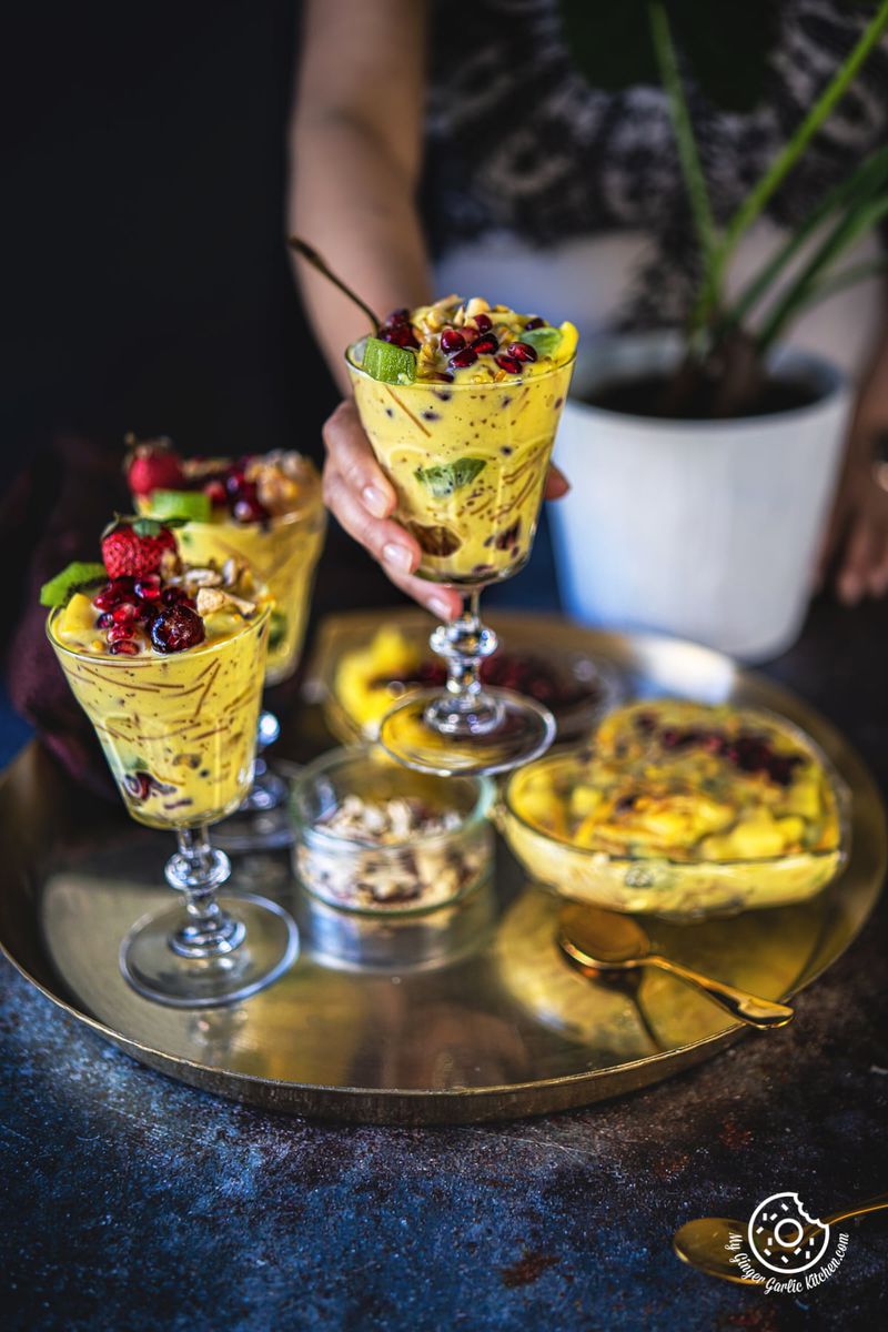 a female holding a vermicelli fruit custard glass and two more glasses kept on a golden plate